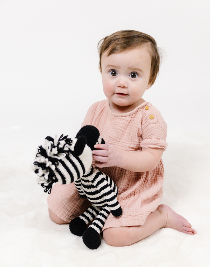 תינוקת אוחזת בבובה סרוגה של זברה בגווני שחור ולבן, מהמותג לחינוך קיימותי