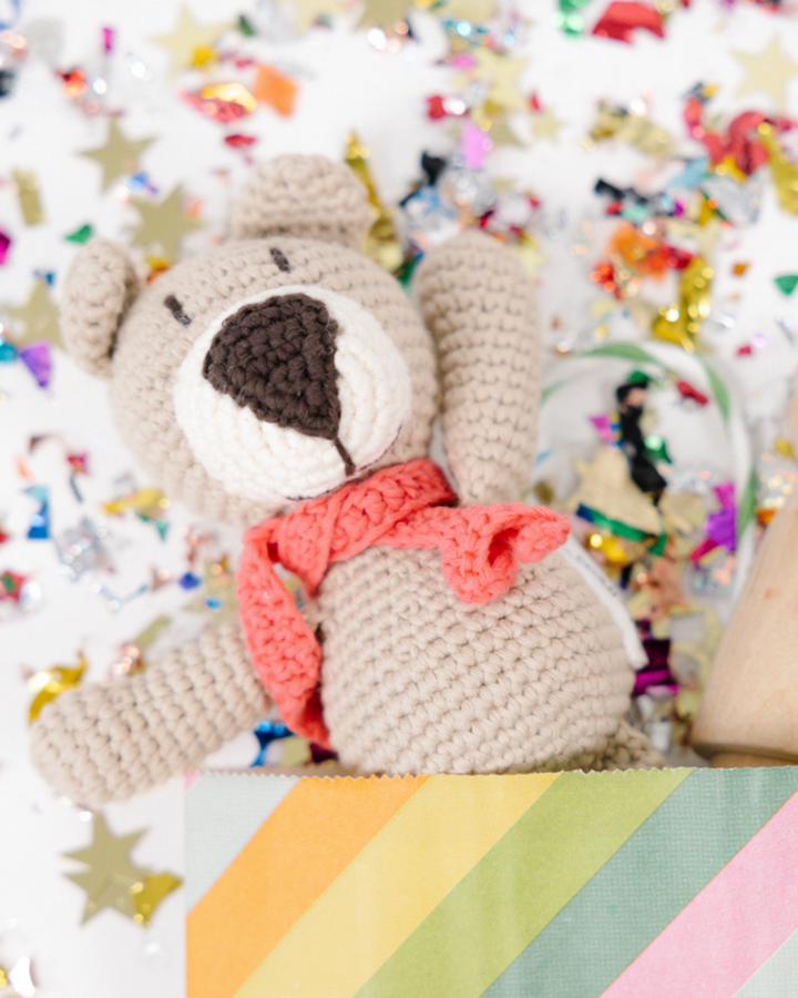 בובת דוב סרוגה בצבע ביז' מונחת על רקע קונפטי - בובות סרוגות יפות
