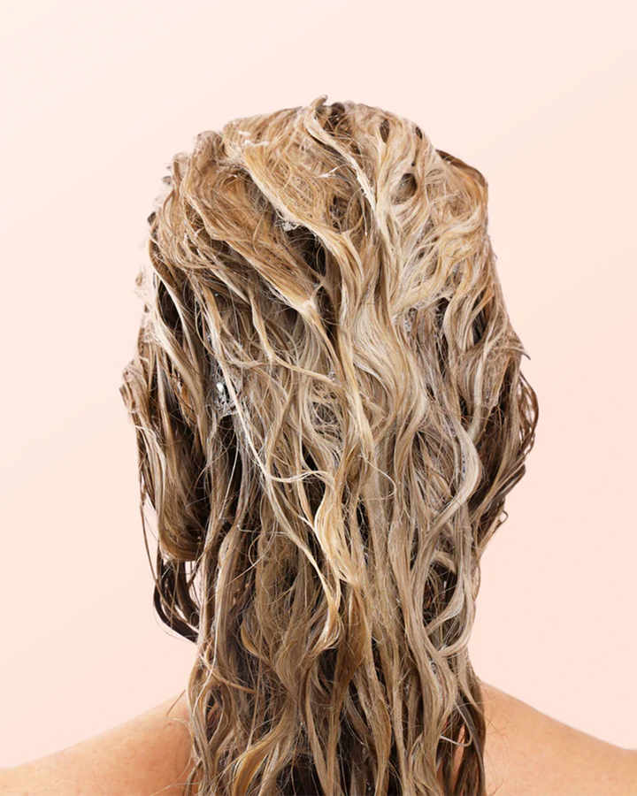 תמונה קרובה של שימוש בשמפו משקם טבעוני על שיער לח ומתולתל למראה מלא ובריא